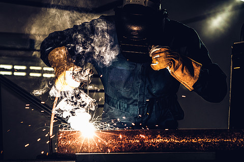 金属焊工与弧焊机一起工作,在工厂焊接钢同时佩戴安全设备通过手工技能劳动概念的金属制品制造?和建筑维护服务
